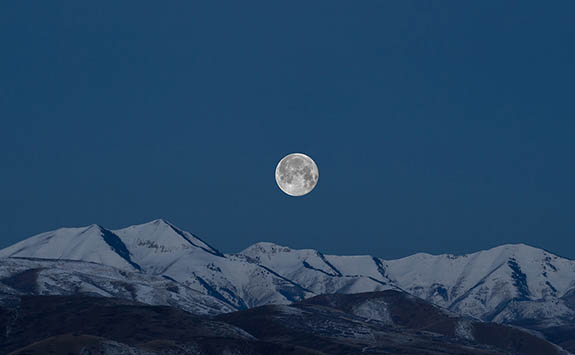 Bright moon at night above snow capped mountains.